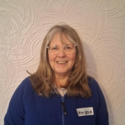 a smiling woman in glasses and a blue fleece top with the gate logo