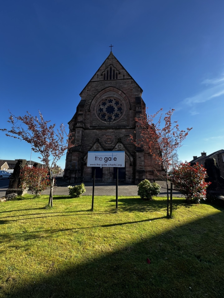 exterior photo of a church and churchyard with a sign aying the gate