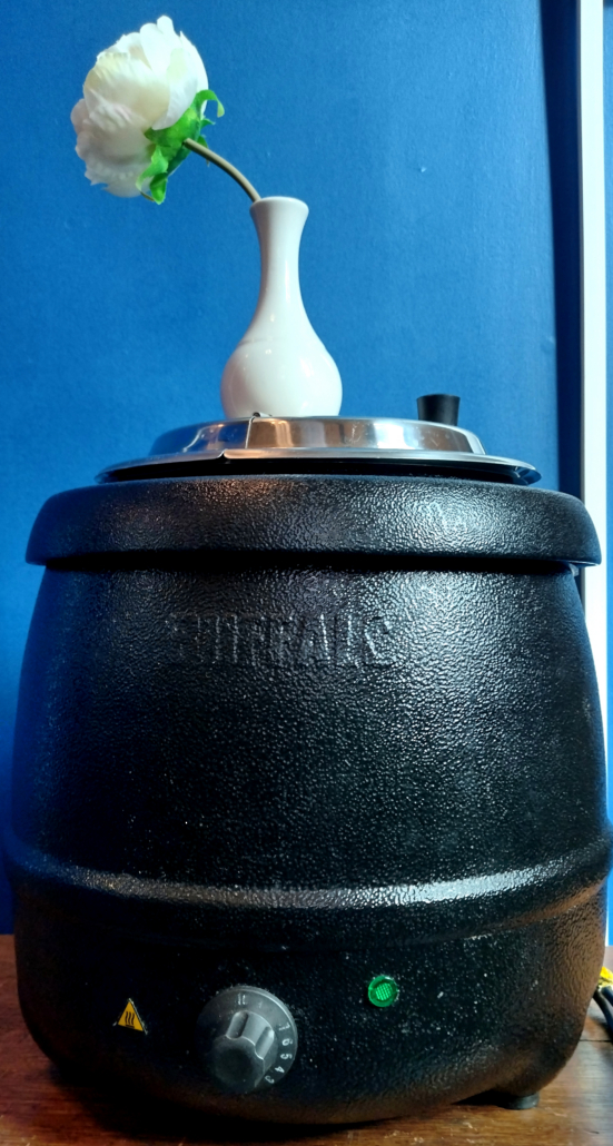 a black soup urn with a white flower in a white vase on top