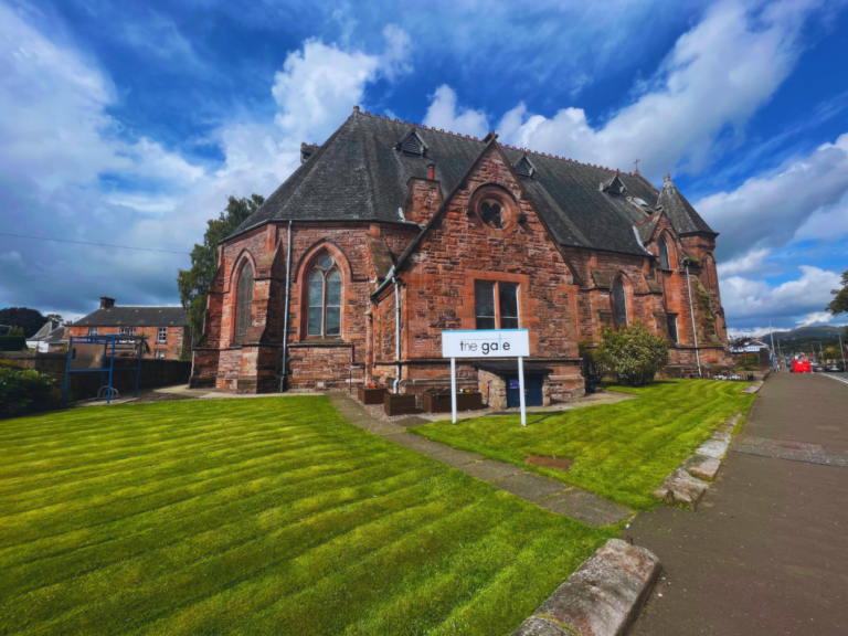 an exterior shot of a church building featuring well kept grounds and a sign reading the gate.